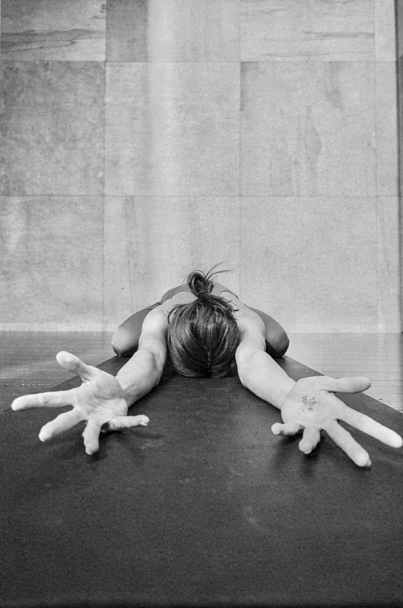 Caitlyne in a deep forward fold on a studio mat, arms outstretched with open hands reaching forward
